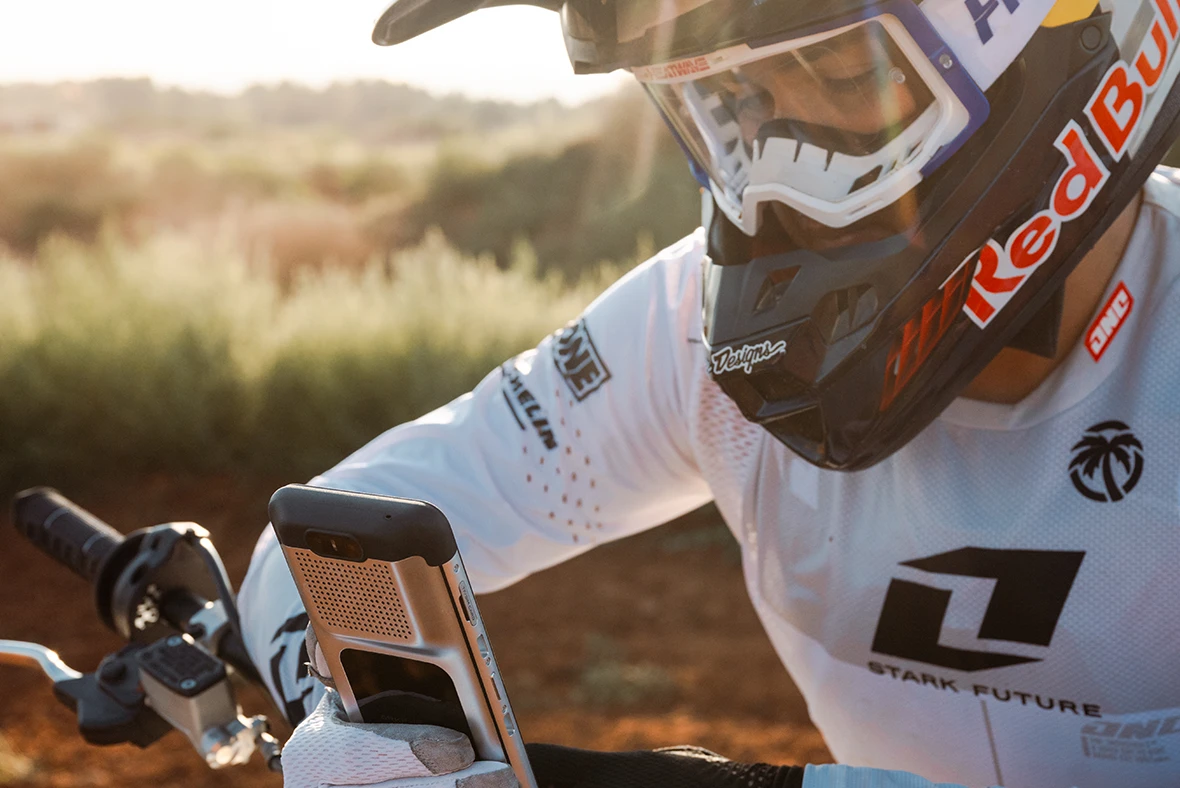 Close-up of a rider in white gear and a helmet leaning over the handlebars of a VARG, with the dashboard between the bars.