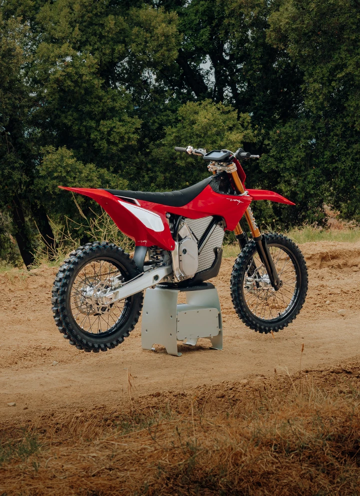 VARG Factory Edition de profil gauche en extérieur — graphismes Factory Red, végétation verte en arrière-plan, moto de motocross électrique ALPHA